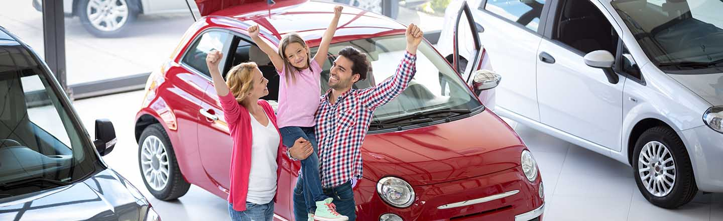 A mother and father holding their daughter up on their shoulders, while they all smile and raise their closed hands up in the air