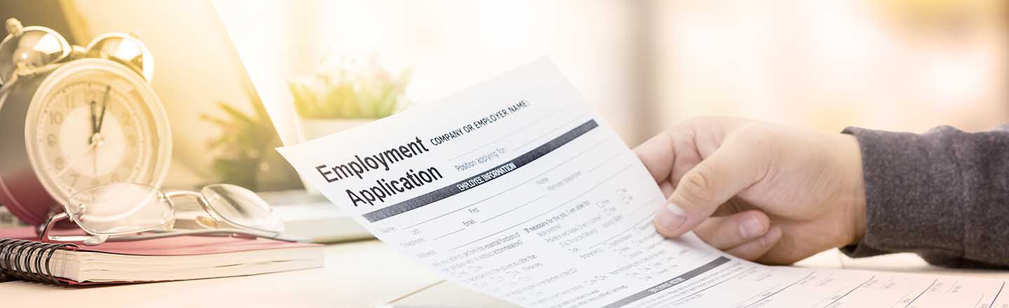 A close up of a hand holding an employment application at a desk