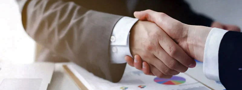 Two hands shaking above finance papers
